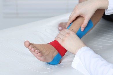 Photo of Doctor applying kinesio tapes to patient's foot in hospital, closeup