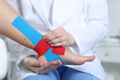 Photo of Doctor applying kinesio tapes to patient's foot in hospital, closeup