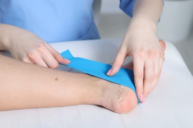 Photo of Doctor applying kinesio tapes to patient's foot in hospital, closeup