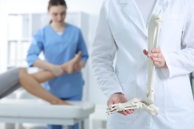 Photo of Doctor examining patient's foot in hospital, focus on medical worker with human leg skeleton