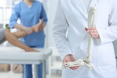 Photo of Doctor examining patient's foot in hospital, focus on medical worker with human leg skeleton