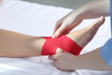 Photo of Doctor applying kinesio tapes to patient's foot in hospital, closeup