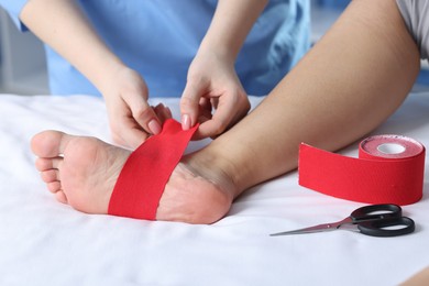 Photo of Doctor applying kinesio tapes to patient's foot in hospital, closeup