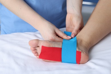 Photo of Doctor applying kinesio tapes to patient's foot in hospital, closeup