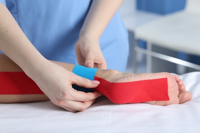 Photo of Doctor applying kinesio tapes to patient's foot in hospital, closeup