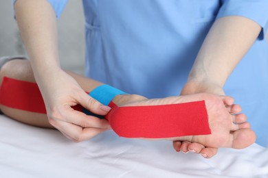 Photo of Doctor applying kinesio tapes to patient's foot in hospital, closeup