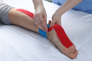 Photo of Doctor applying kinesio tapes to patient's foot in hospital, closeup