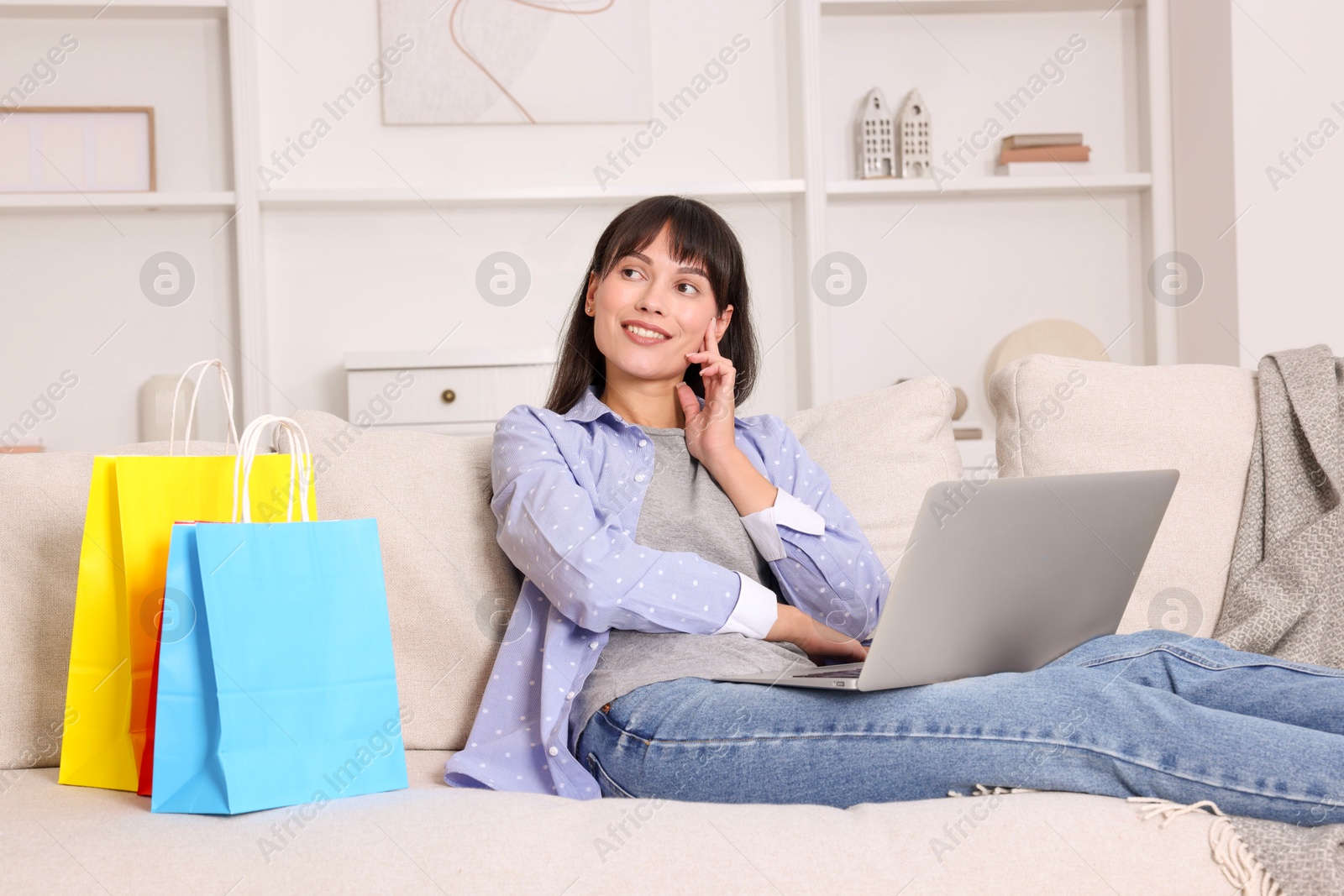 Photo of Internet shopping. Happy woman with laptop and colorful bags on sofa at home