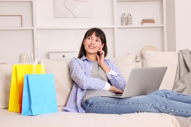 Photo of Internet shopping. Happy woman with laptop and colorful bags on sofa at home