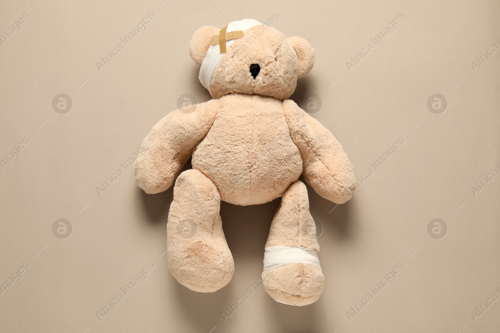 Teddy bear with bandages and sticking plasters on beige background, top view Photo of Teddy bear with bandages and sticking plasters on beige background, top view