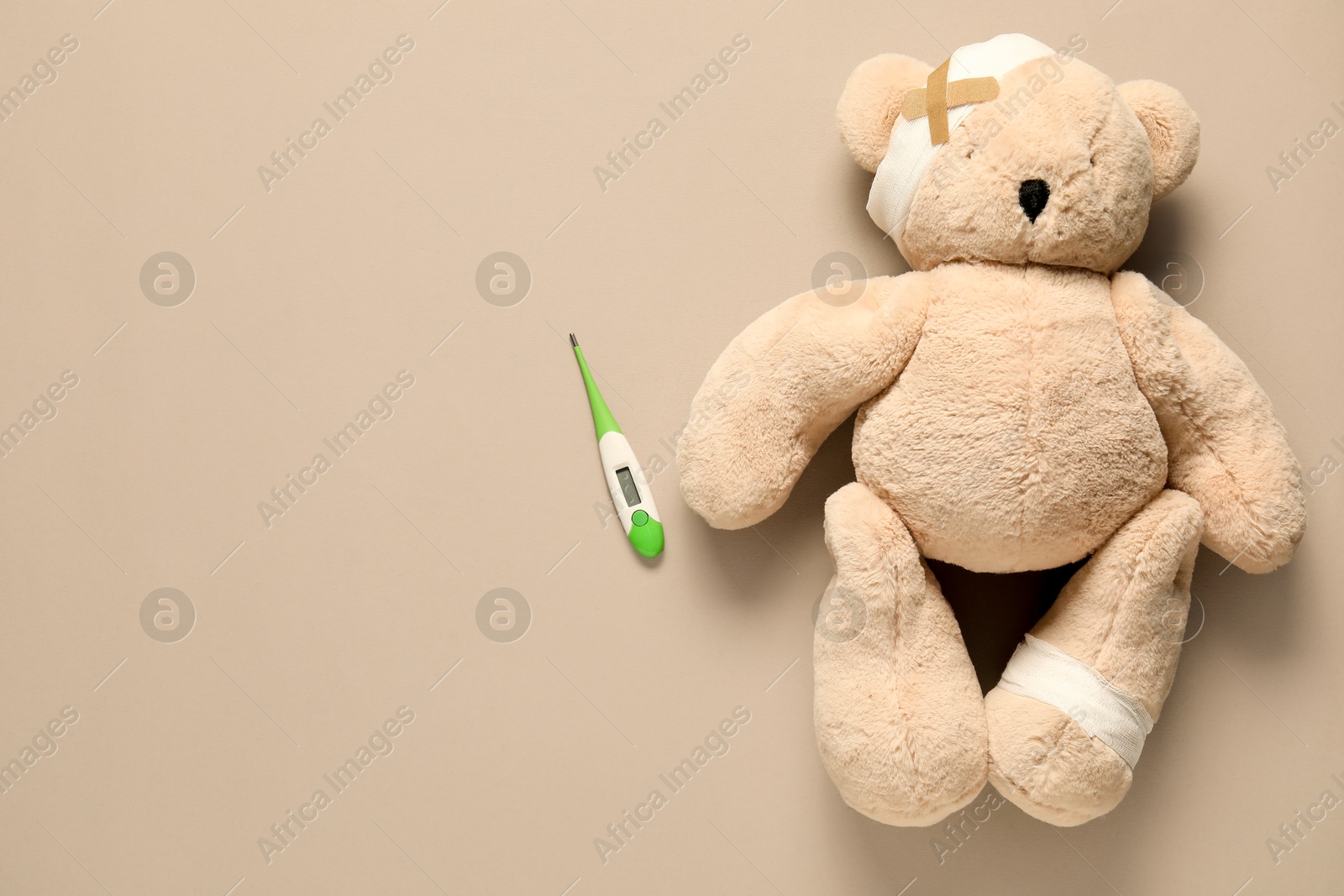 Teddy bear with bandages, thermometer and sticking plasters on beige background, top view. Space for text Photo of Teddy bear with bandages, thermometer and sticking plasters on beige background, top view. Space for text