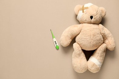 Photo of Teddy bear with bandages, thermometer and sticking plasters on beige background, top view. Space for text