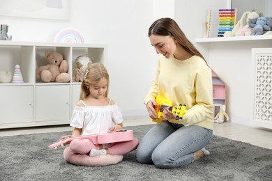 Photo of Young woman teaching little girl to play ukulele at home