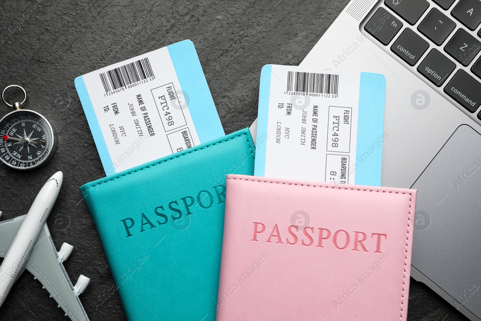 Photo of Travel agency. Flight tickets, passports, plane model, compass and laptop on dark textured table, flat lay