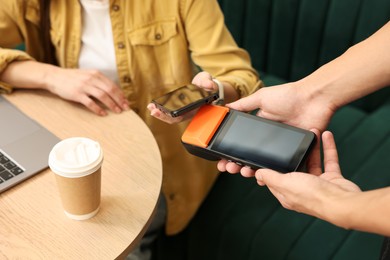 Photo of Woman paying with smartphone via terminal in cafe, closeup