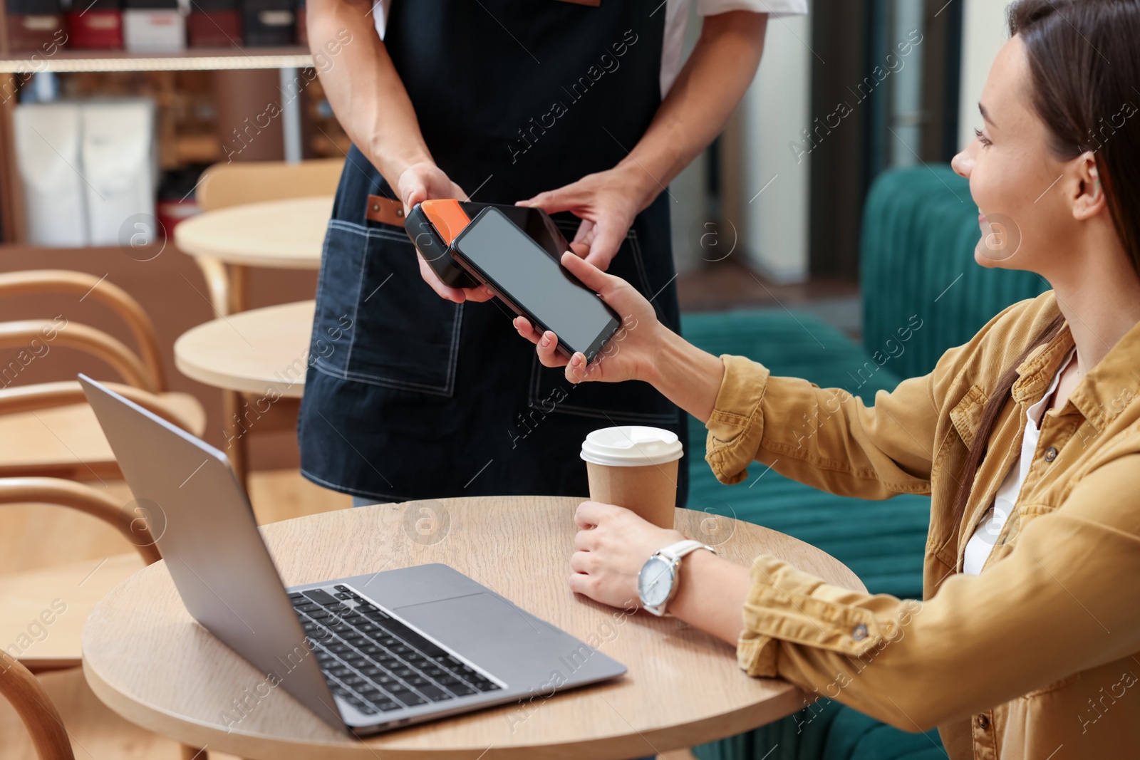 Photo of Woman paying with smartphone via terminal at wooden table in cafe