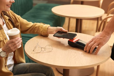 Photo of Woman paying with smartphone via terminal at wooden table in cafe, closeup