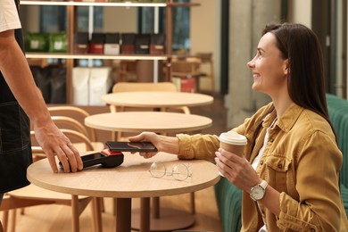 Photo of Woman paying with smartphone via terminal at wooden table in cafe