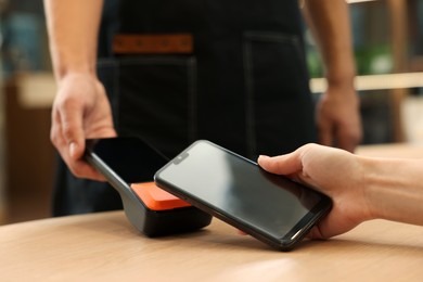 Photo of Woman paying with smartphone via terminal at wooden table in cafe, closeup