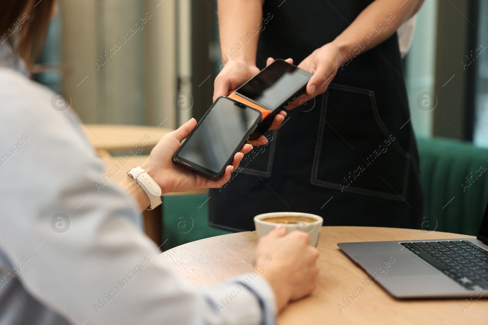 Photo of Woman paying with smartphone via terminal at wooden table in cafe, closeup