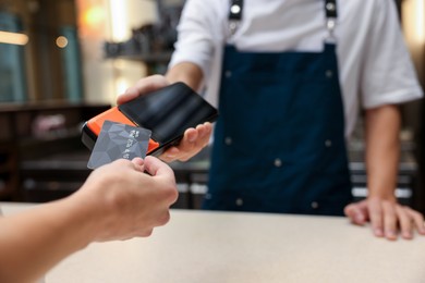 Photo of Woman paying with credit card via terminal in cafe, closeup