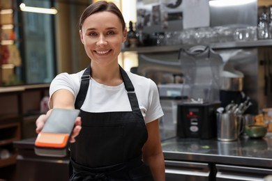 Photo of Smiling cafe worker with payment terminal indoors