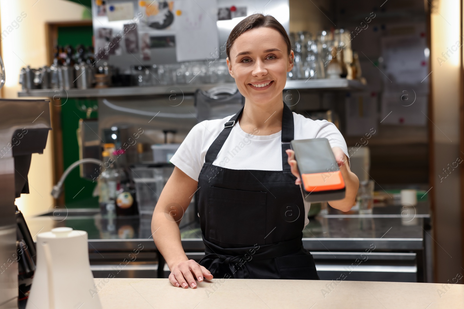 Photo of Smiling cafe worker with payment terminal indoors