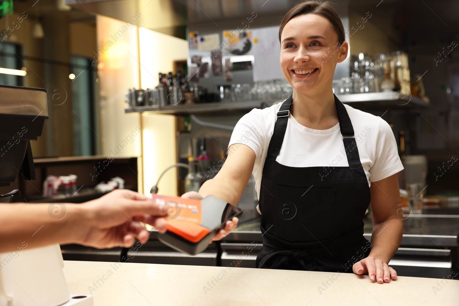 Photo of Cafe worker taking payment from client via terminal indoors