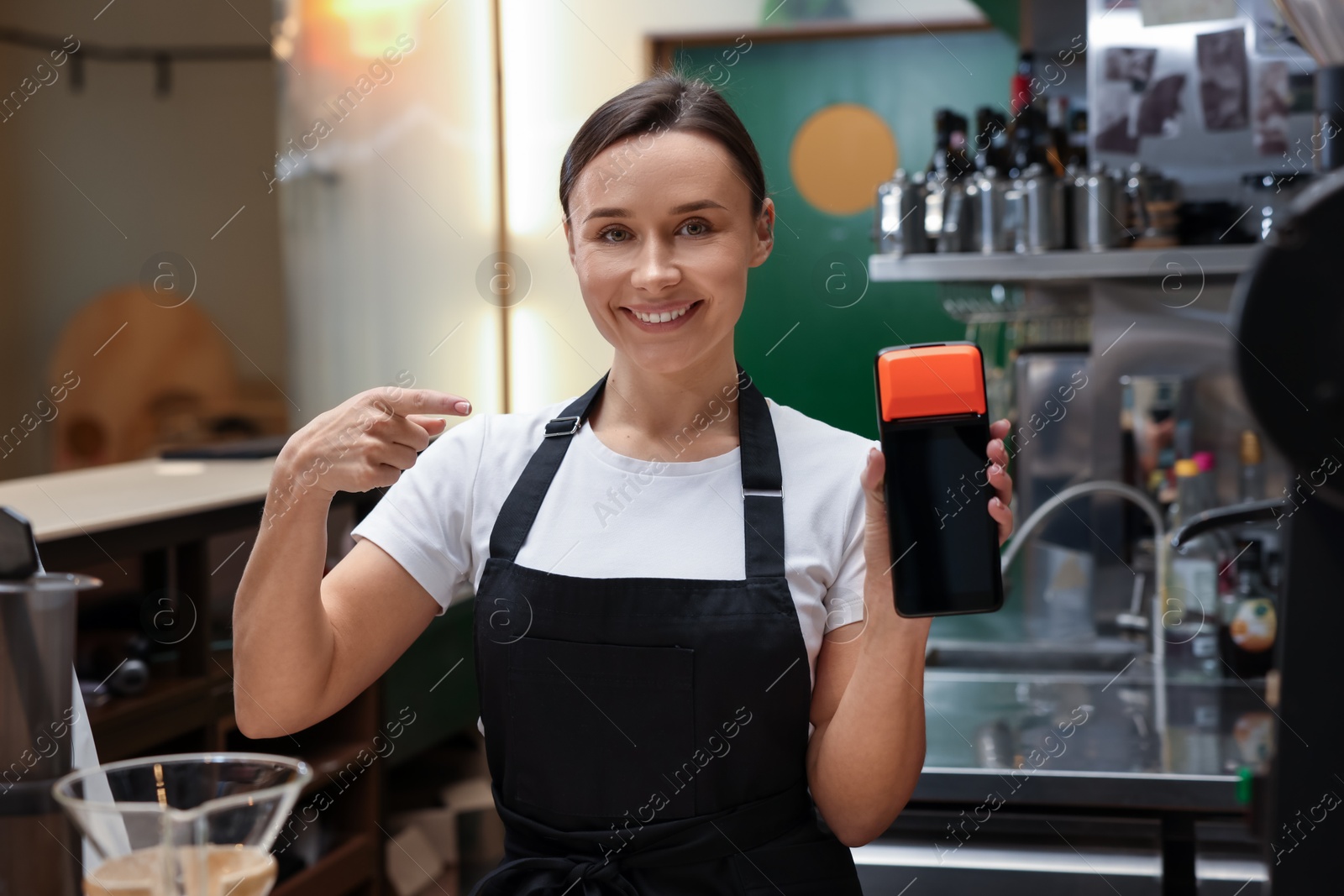 Photo of Smiling cafe worker pointing at payment terminal indoors