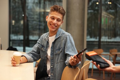 Photo of Man paying with smartphone via terminal in cafe