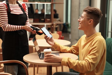 Photo of Man paying with smartphone via terminal at wooden table in cafe