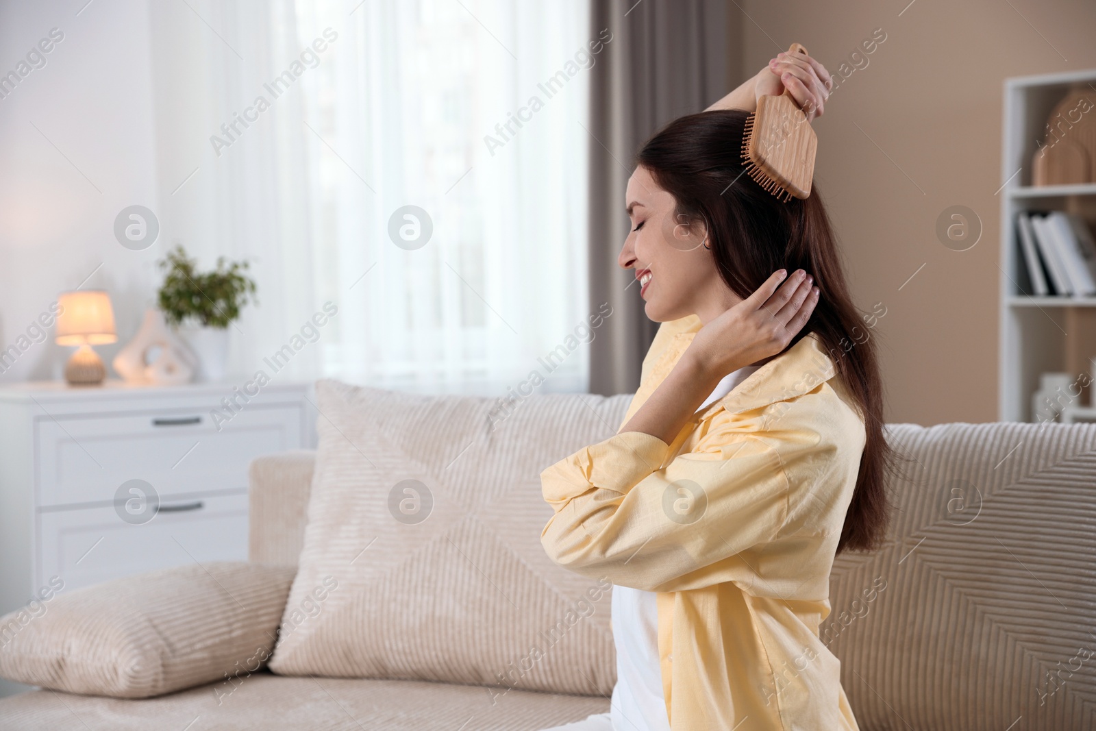 Photo of Smiling woman brushing her hair at home, space for text