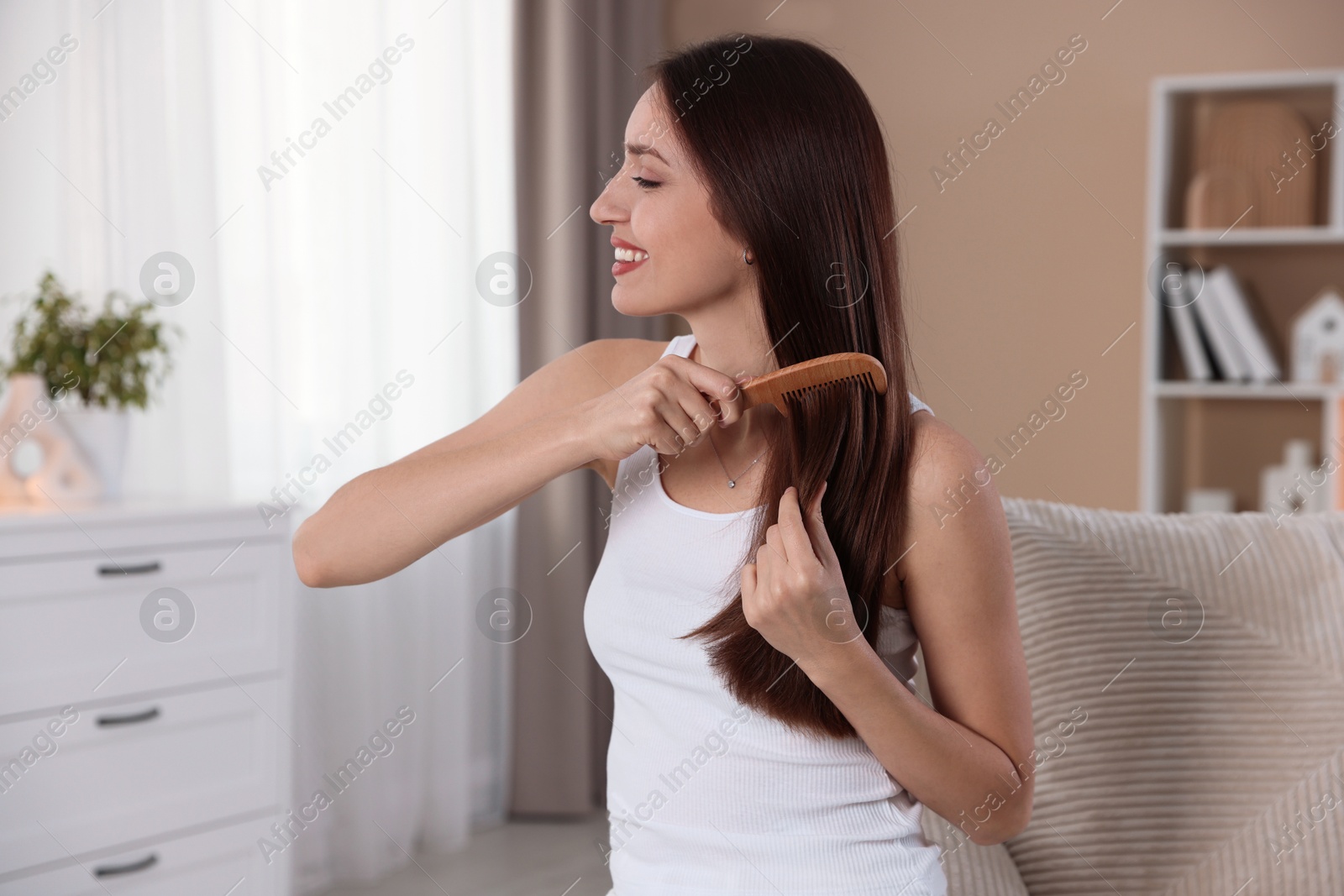 Photo of Smiling woman brushing her hair with comb at home