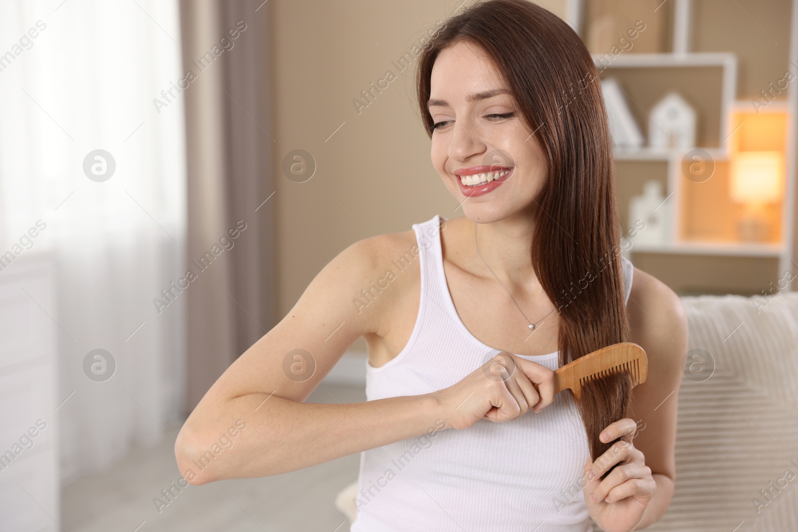 Photo of Smiling woman brushing her hair with comb at home