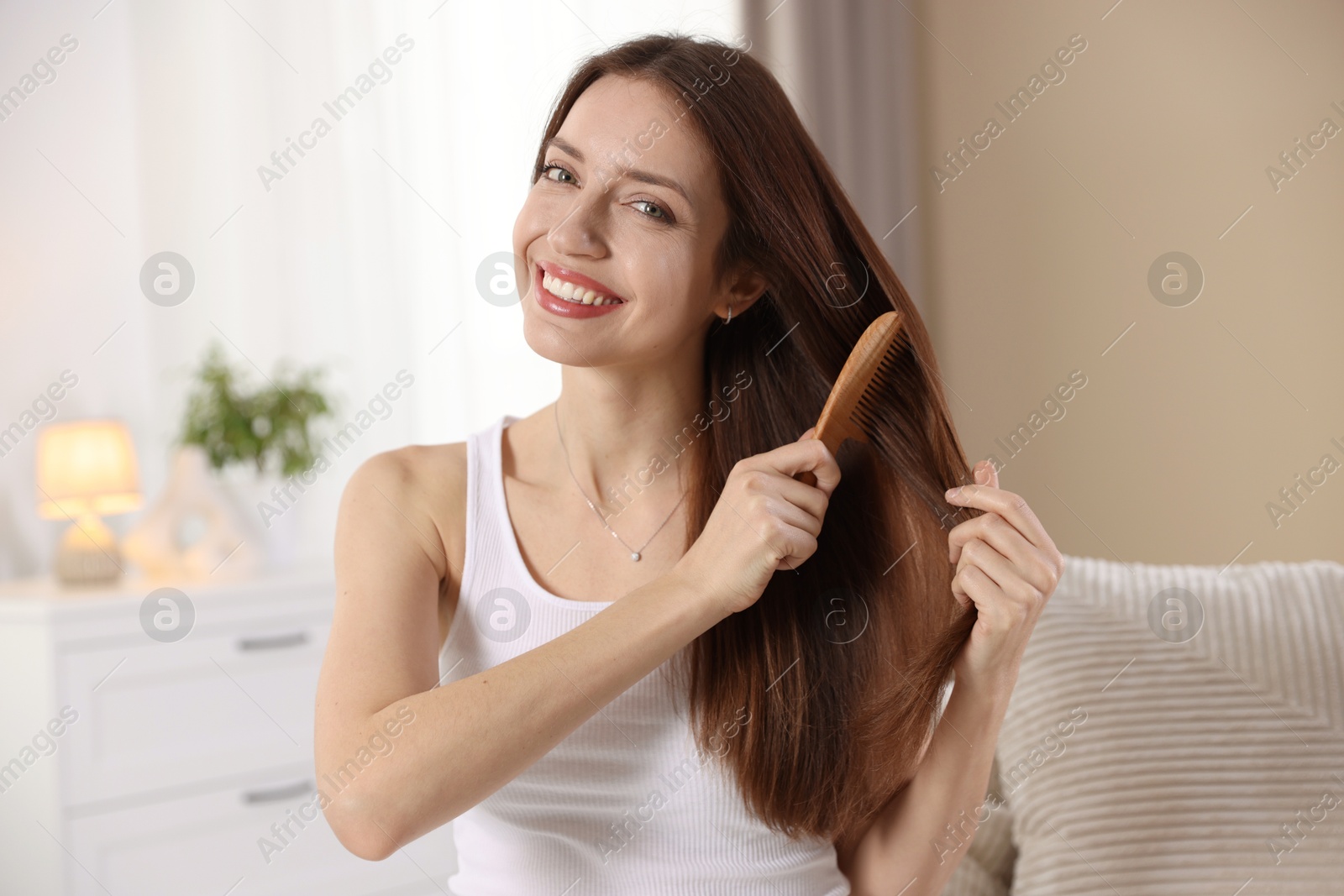 Photo of Smiling woman brushing her hair with comb at home