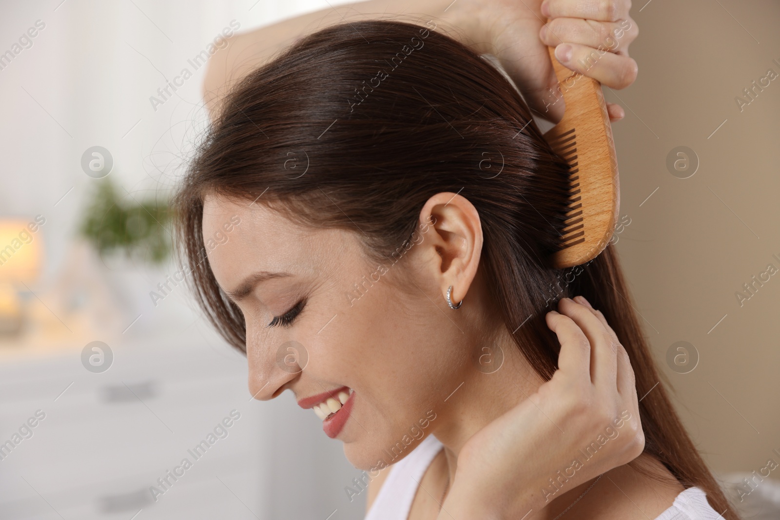 Photo of Woman brushing her hair with comb at home, closeup