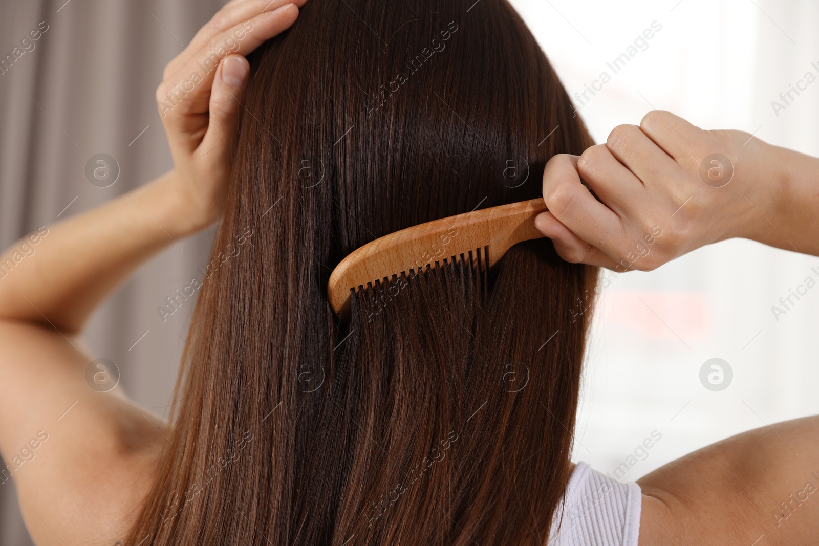 Photo of Woman brushing her hair with comb indoors, closeup