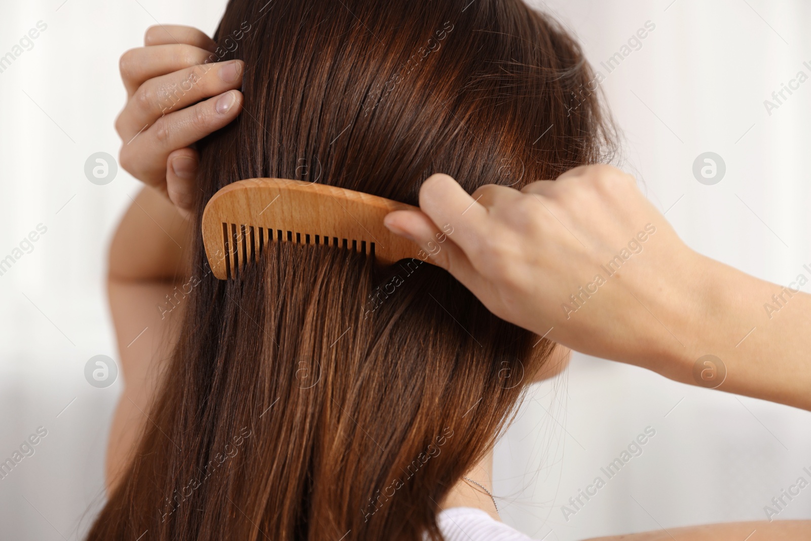 Photo of Woman brushing her hair with comb indoors, closeup