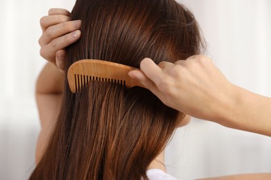 Photo of Woman brushing her hair with comb indoors, closeup