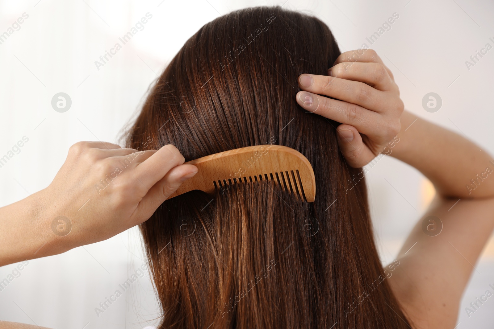 Photo of Woman brushing her hair with comb indoors, closeup