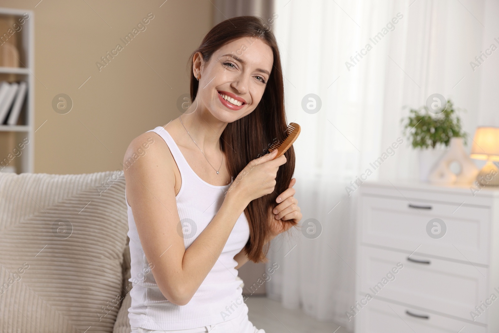 Photo of Smiling woman brushing her hair with comb at home