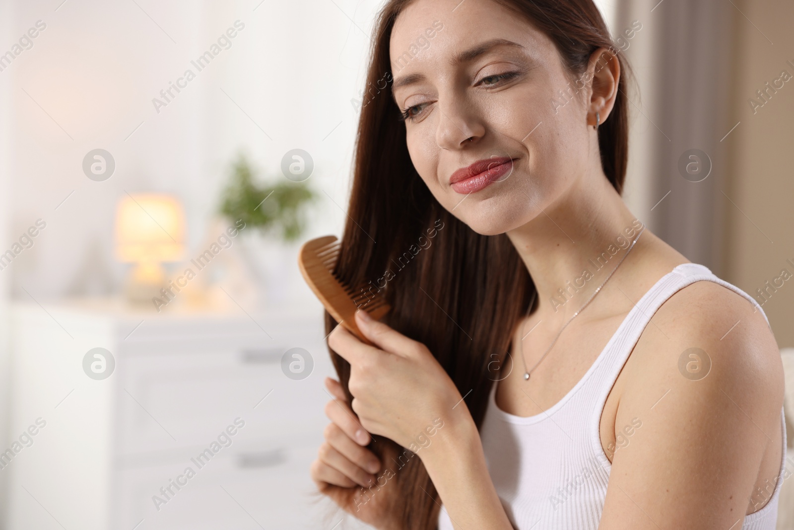 Photo of Beautiful woman brushing her hair with comb at home, space for text