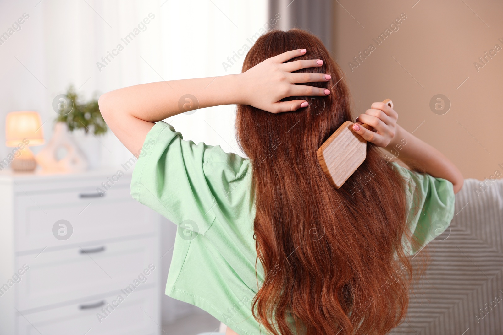 Photo of Teenage girl brushing her hair at home, back view