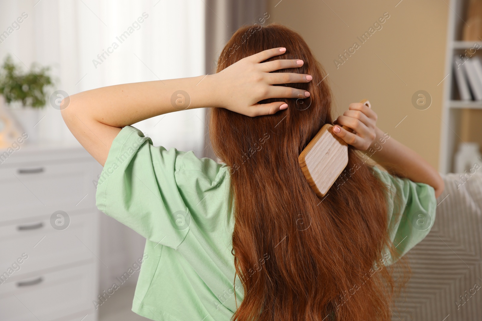 Photo of Teenage girl brushing her hair at home, back view