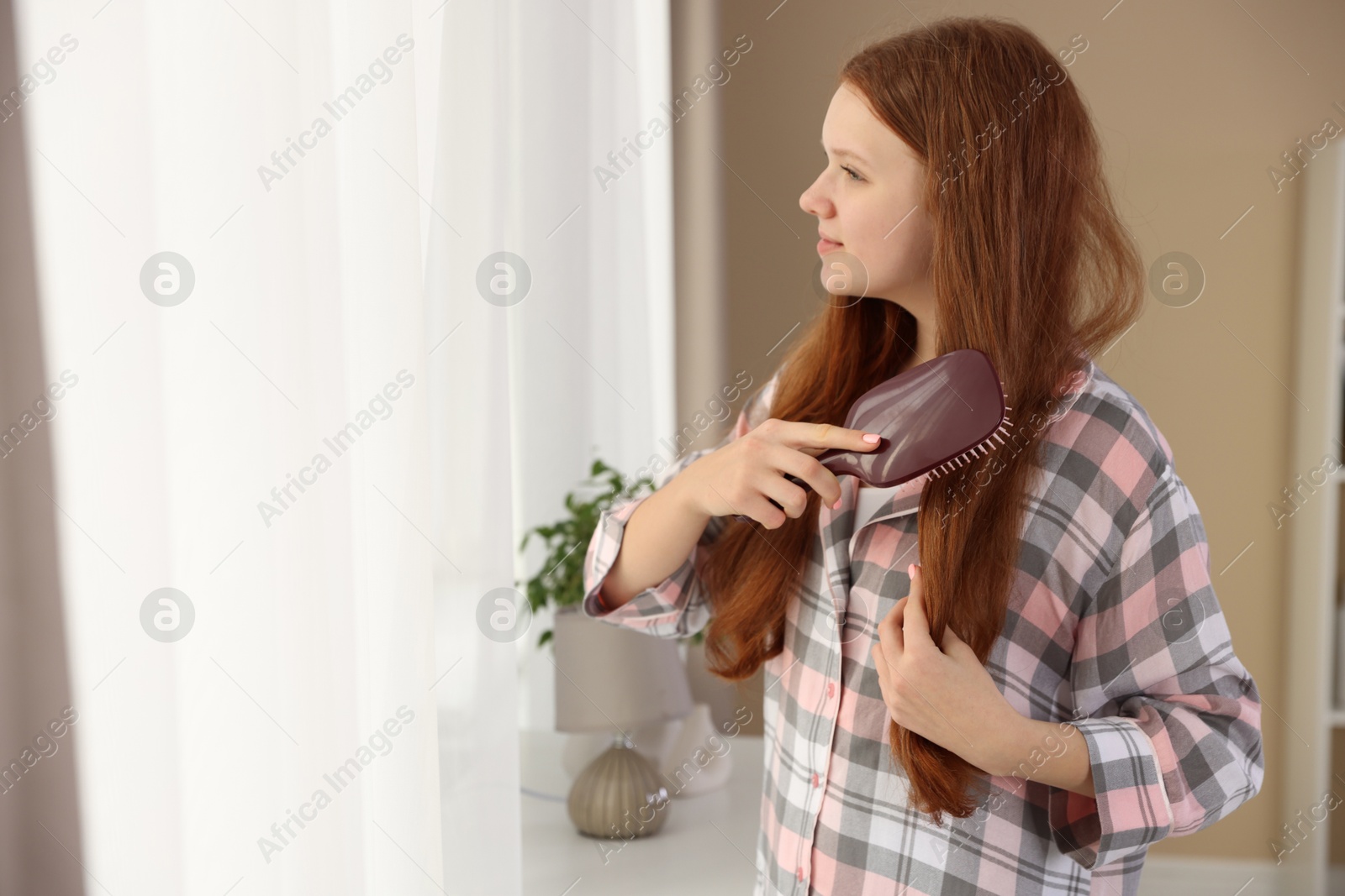 Photo of Beautiful teenage girl brushing her hair at home, space for text