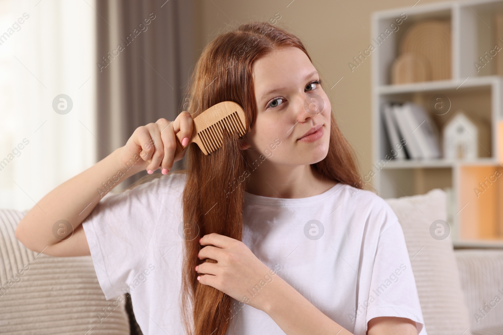 Photo of Beautiful teenage girl brushing her hair with comb at home