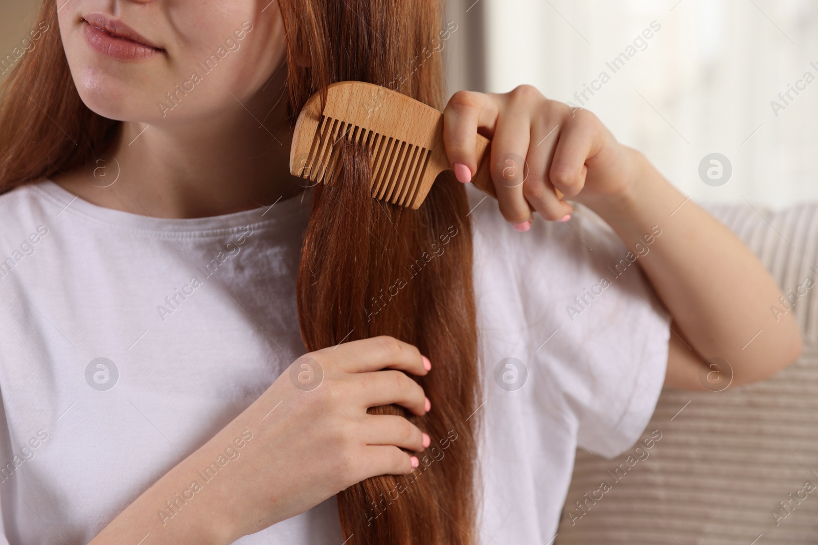 Photo of Teenage girl brushing her hair with comb at home, closeup