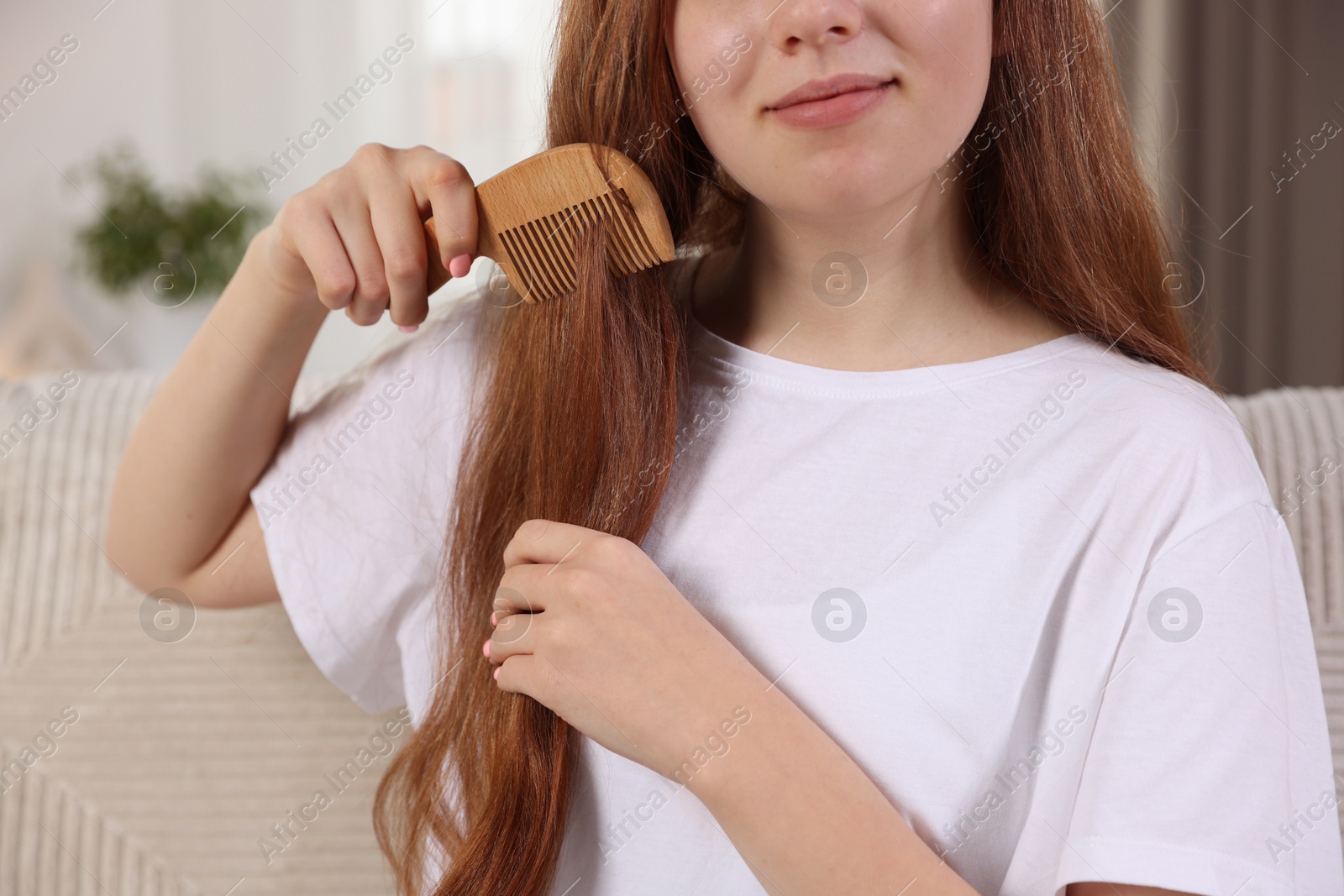 Photo of Teenage girl brushing her hair with comb at home, closeup