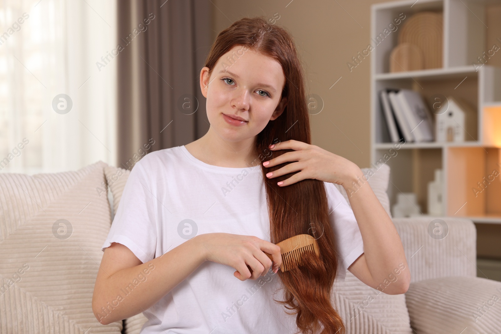 Photo of Beautiful teenage girl brushing her hair with comb at home