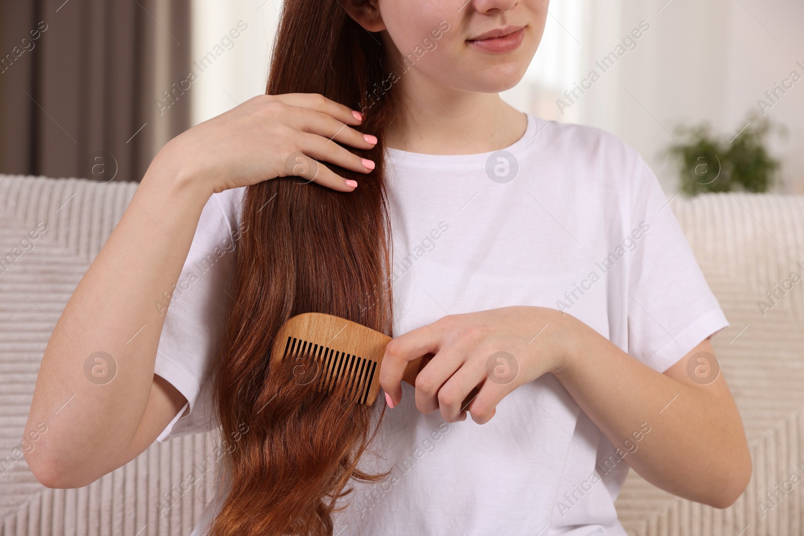 Photo of Teenage girl brushing her hair with comb at home, closeup